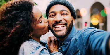 Woman clinging to mans side, embracing a big kiss on the cheek. 