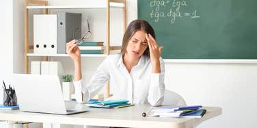 stressed teacher sitting at her desk in front of a blackboard