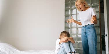 angry mother yelling at her little girl who is on the bed with her face covered