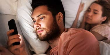 Man emotionally cheating late at night on phone, while wife is in bed next to him.