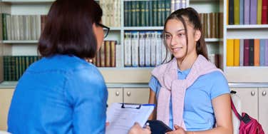 high school teen girl talking with teacher in classroom