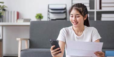 young woman calculating bill totals with paper and phone