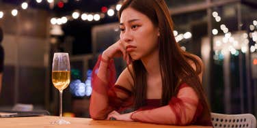 sad woman sitting alone at bar with glass of wine