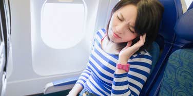 Woman sitting in economy airplane seat looking annoyed. 