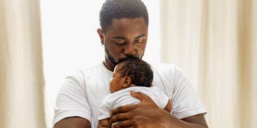 Loving and caring black father giving a hug to his newborn baby daughter at home