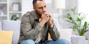 young man sitting thoughtfully and upset at home on the couch.