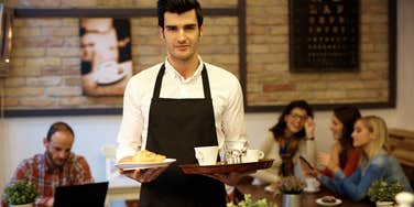 Waiter looking serious while carrying trays of food