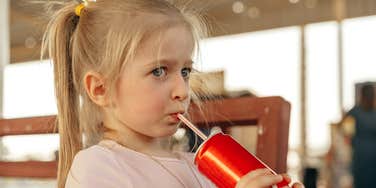 Little girl drinking out of a straw on school playground