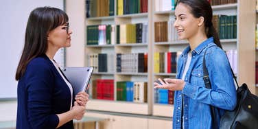 high school student talking to teacher inside classroom