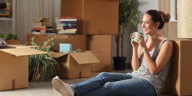 Happy tenant resting drinking coffee moving home sitting on the floor in the night