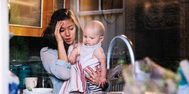 Wife stressed out standing in kitchen with baby.