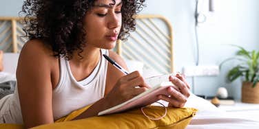 woman laying in bed writing in journal