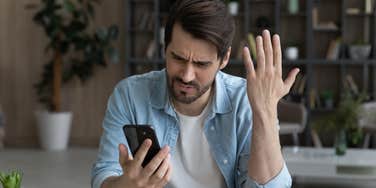 man looking at his phone angry and frowning