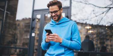 man wearing blue sweatshirt standing outside cafe texting