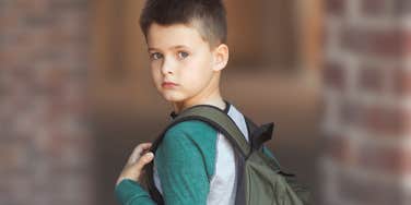 Young boy with a backpack standing in front of his school.