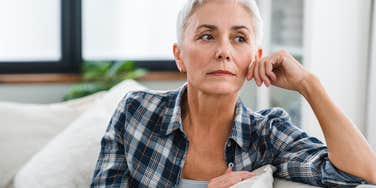 Older woman looking upset while staring out her window.