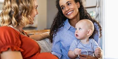 Mixed race woman with expecting mother talking and playing with baby