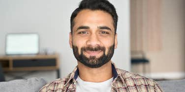 Headshot portrait of confident man looking at camera sitting on couch at modern living room