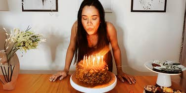 Woman blowing out birthday candle, celebrating childhood pagan tradition.