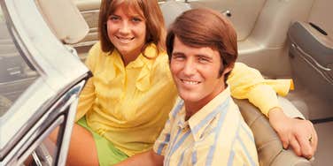 Baby boomer couple in the 70's sitting in car. 