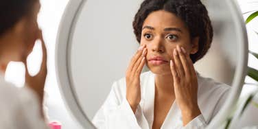 Millennial woman looking at aging skin in mirror. 