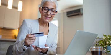 Older woman smiling and doing bills on her laptop.