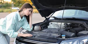 worried woman looking under hood of car 