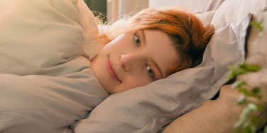 Sleepy woman waking up from dreaming in comfortable white bed smiling 