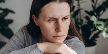 Upset woman leaning her head in her hands and looking out a window.