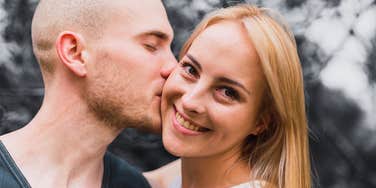  Young couple kisses on the cheek.