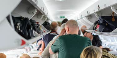 airline passengers standing and sitting while waiting to deplane