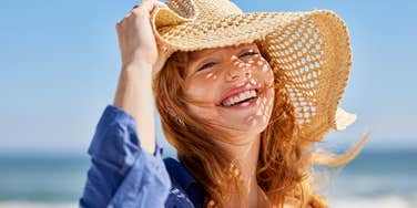 Woman living her life to the fullest wearing hat on the beach and smiling