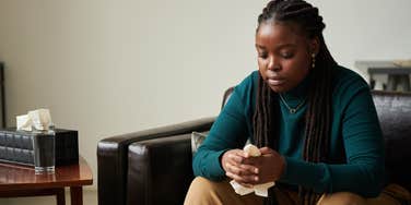 upset woman sitting on couch with tissue in hand