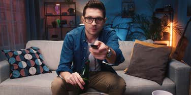 man sitting on couch holding remote watching TV