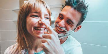 Young married couple having fun playing with shaving foam in the bathroom