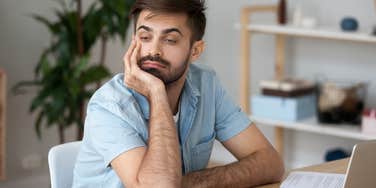 Annoyed Gen Z man looking away from his laptop at his desk.