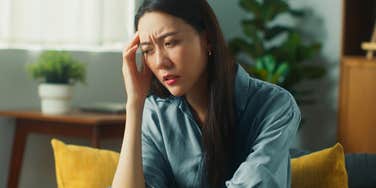 Sad woman sitting on her couch looking at the ground.