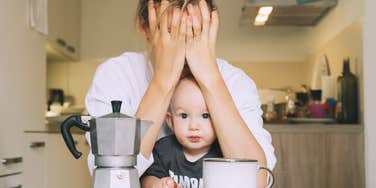 Exhausted woman with baby is sitting with coffee in kitchen