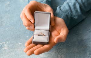 man holding a box with engagement ring in it over blue background