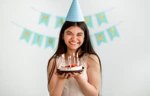 young girl holding cake in front of happy birthday sign
