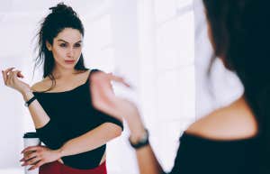 Brunette girl in tracksuit looking at mirror satisfied with body shape