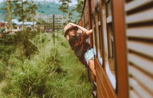  young woman hanging off the side of a train in the countryside