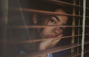 Woman looking sadly out her blinds 