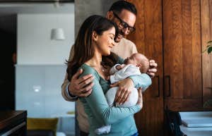 Portrait of young mother and father smiling while holding newborn baby in their home